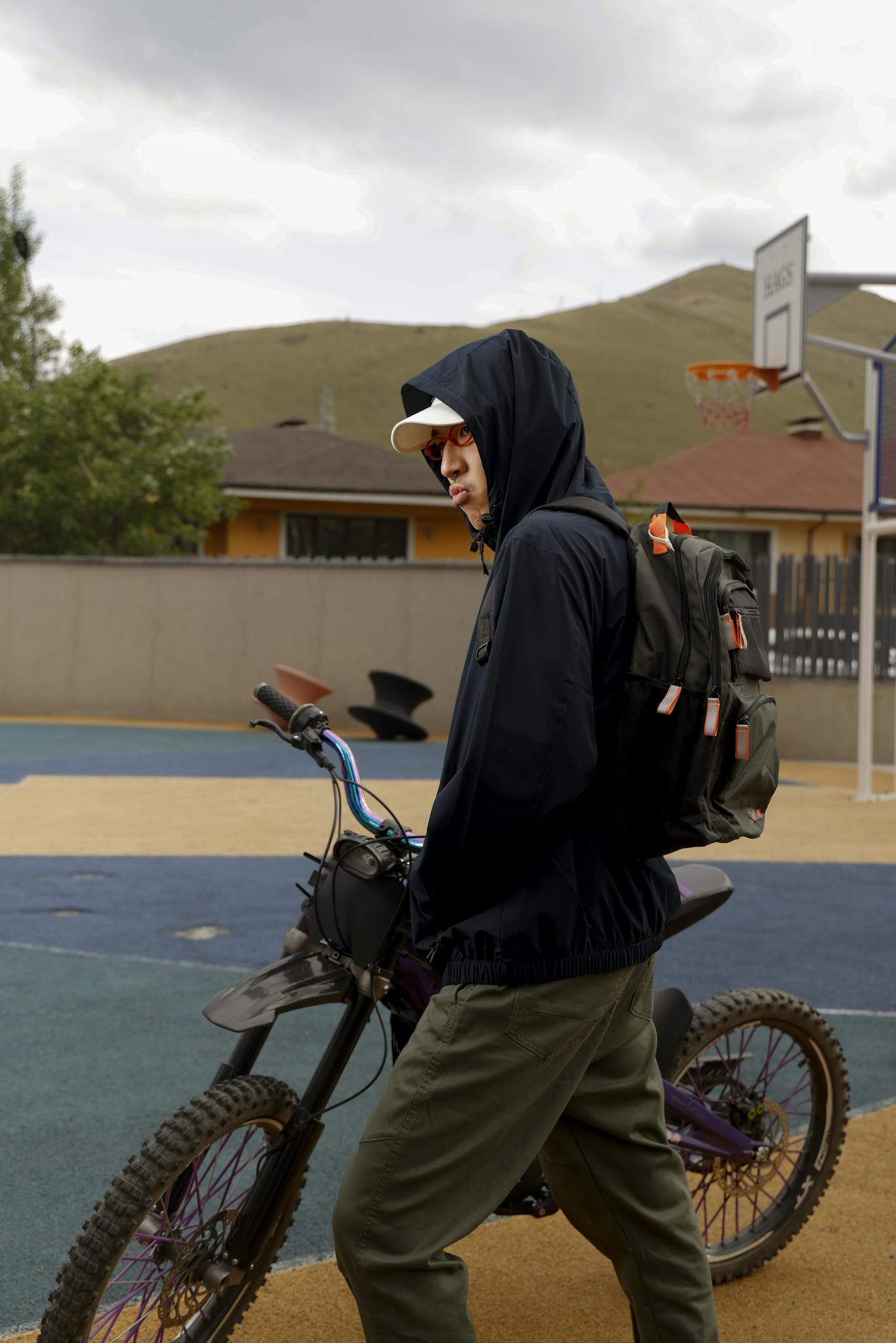 Teenager with a hood on a bike in a playground setting, showcasing urban lifestyle.